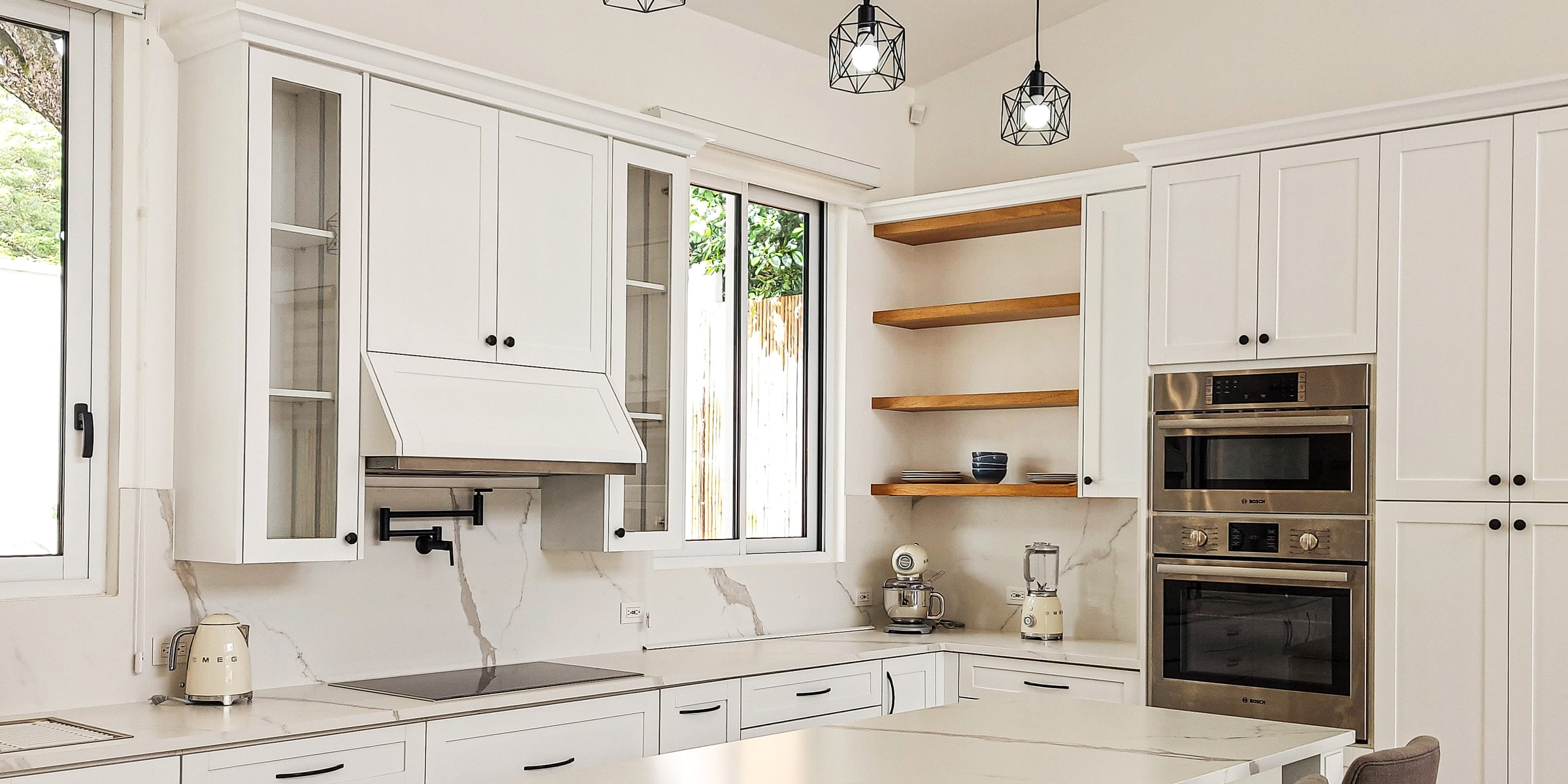 White kitchen with marble backsplash, open wood shelves and black pendant lights