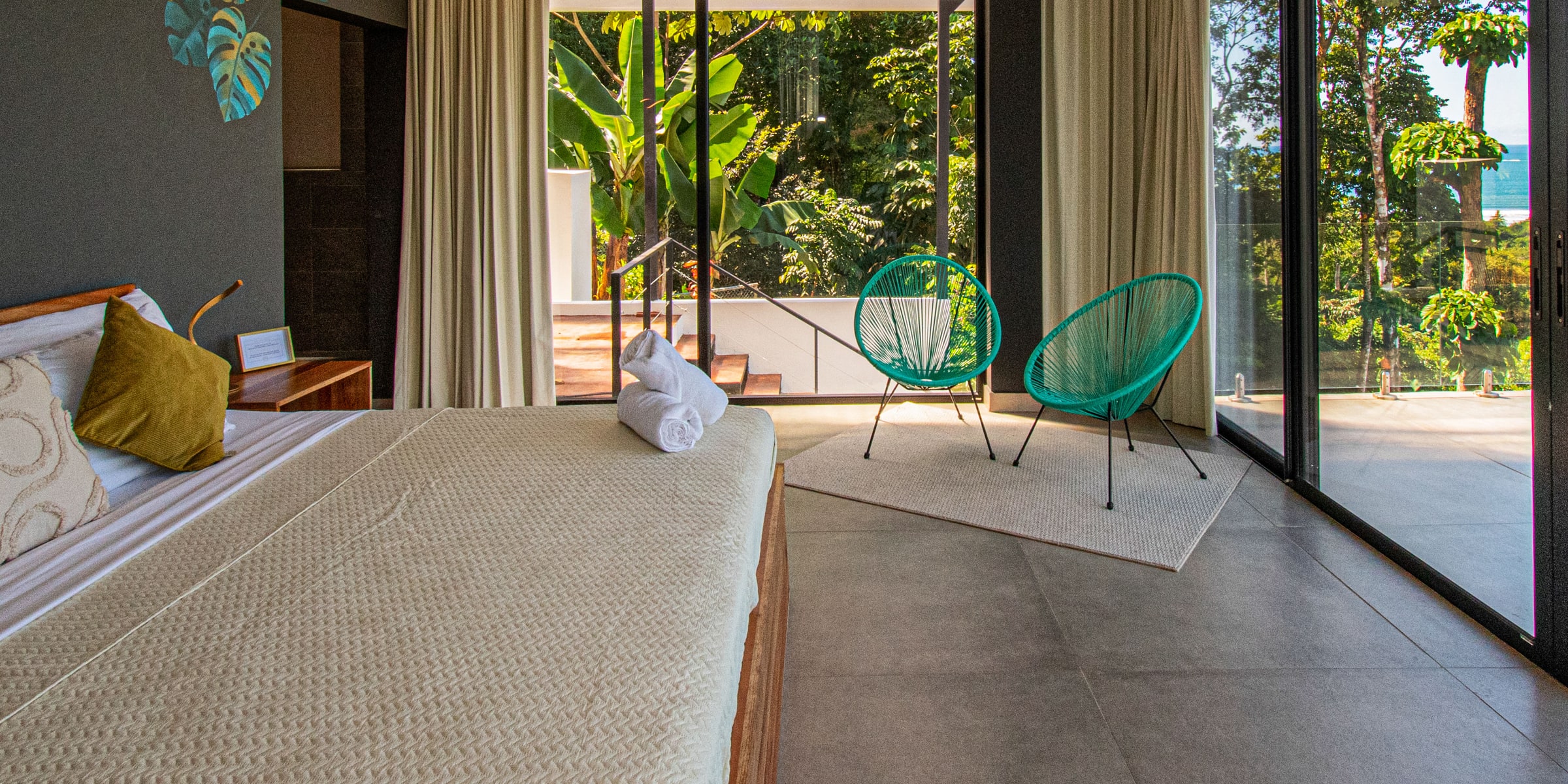Villa Unique bedroom with botanical mural, teal chairs and glass doors to the jungle
