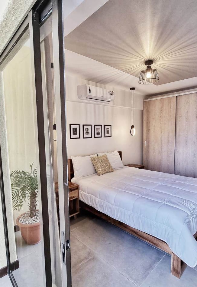Coco Sunset Hills bedroom with white linens, a palm plant and a glass door to the terrace
